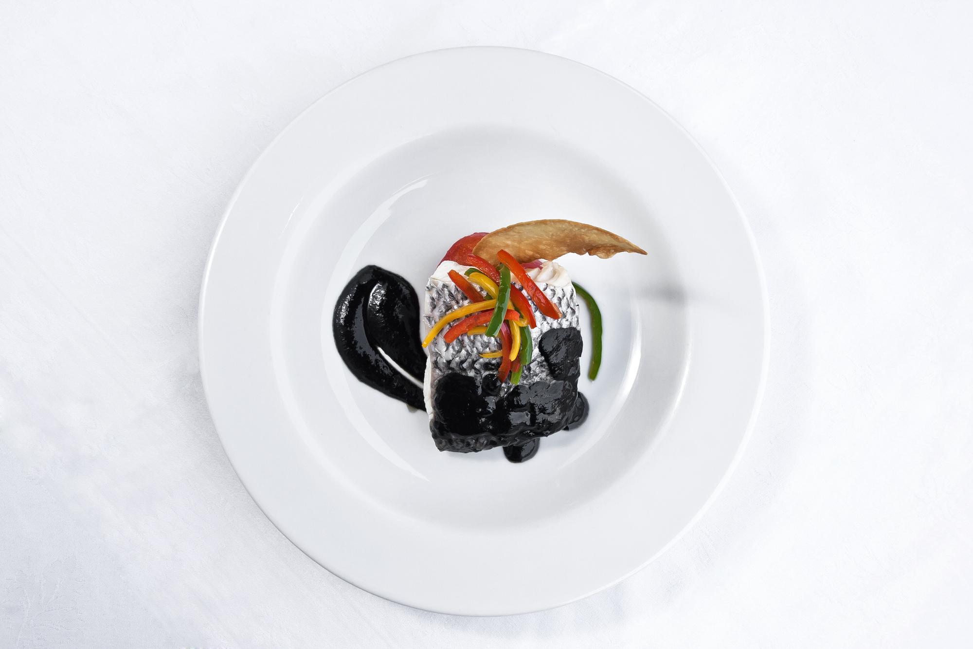 Chef plating a modern tasting dish on dark plate
